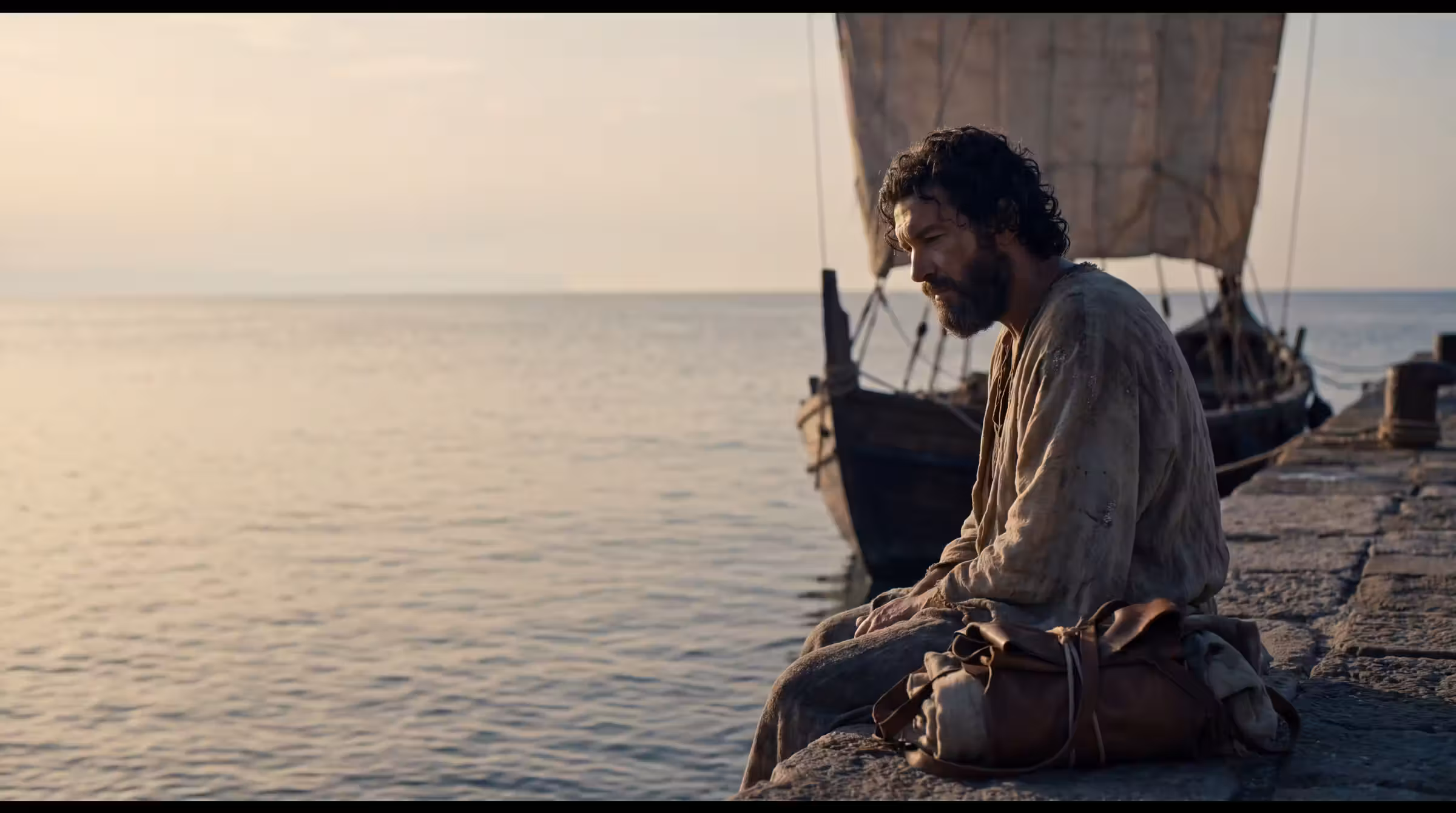 Jonah sitting on the quay at Joppa at dawn, a bundle at his feet, a merchant ship moored beyond him