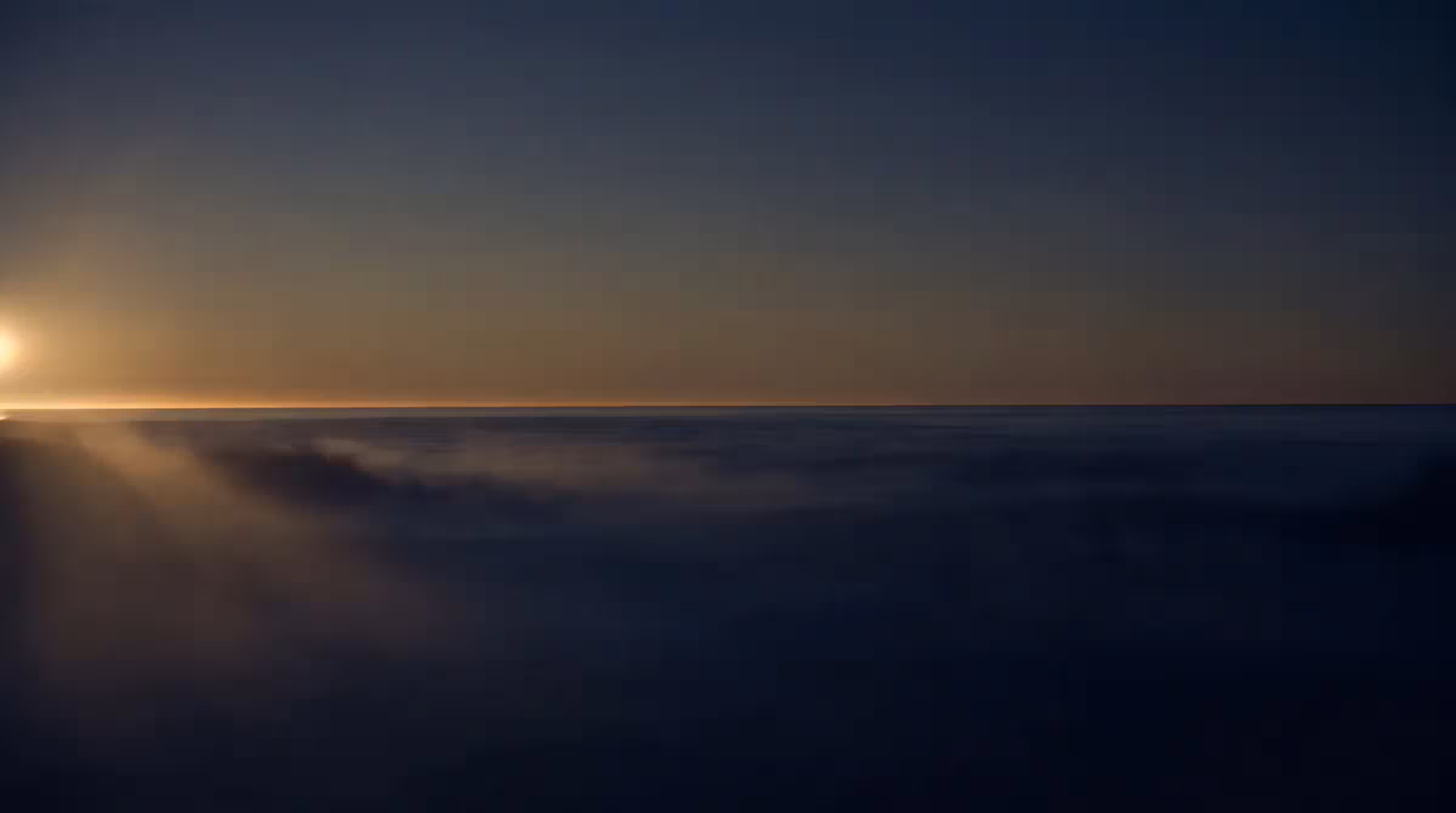 First light breaking along the horizon of a dark, still ocean under a vast empty sky