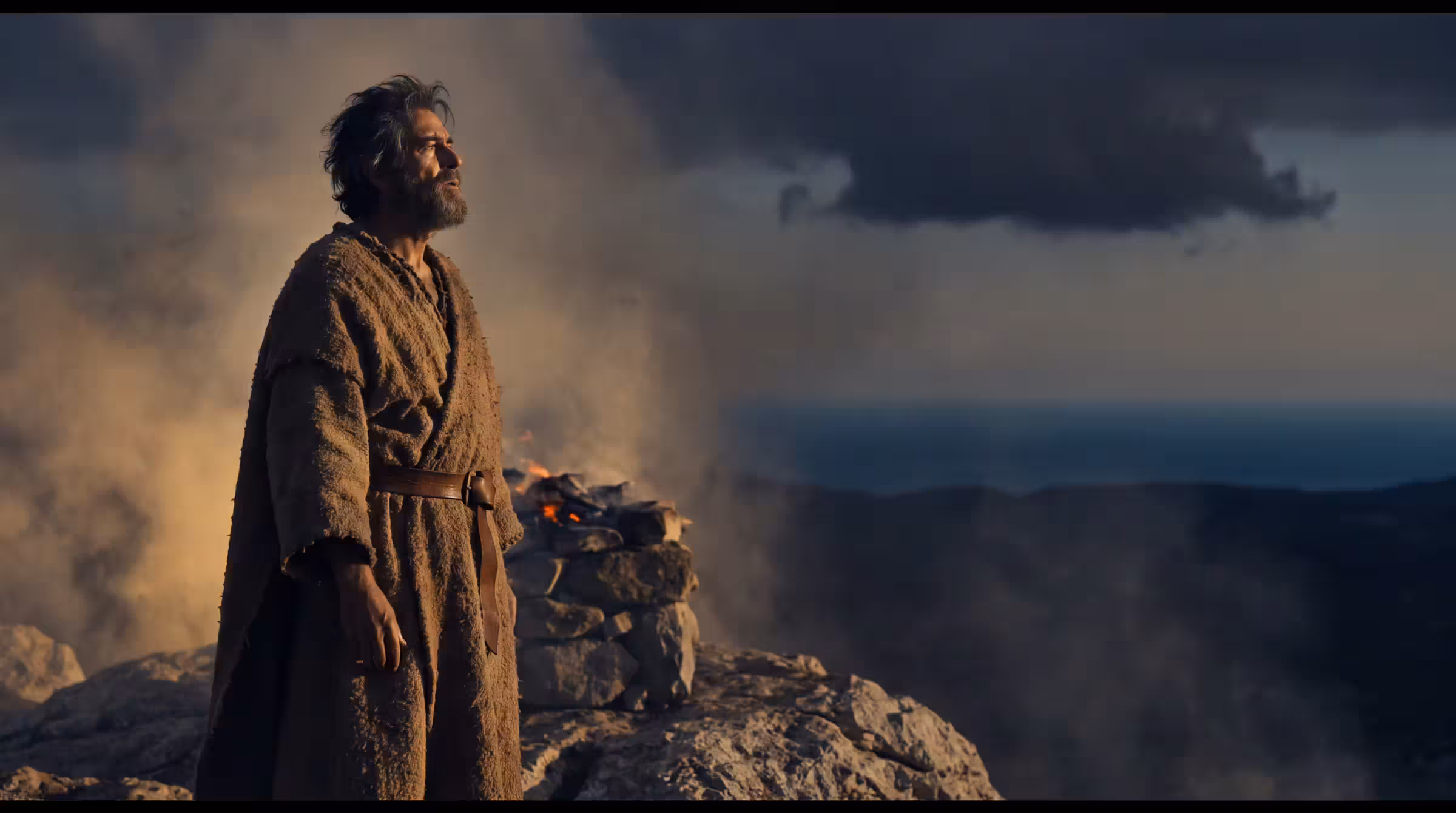 A weathered prophet in a camel-hair cloak on the bare summit of Mount Carmel, a stone altar smouldering behind him and storm cloud gathering over the distant sea