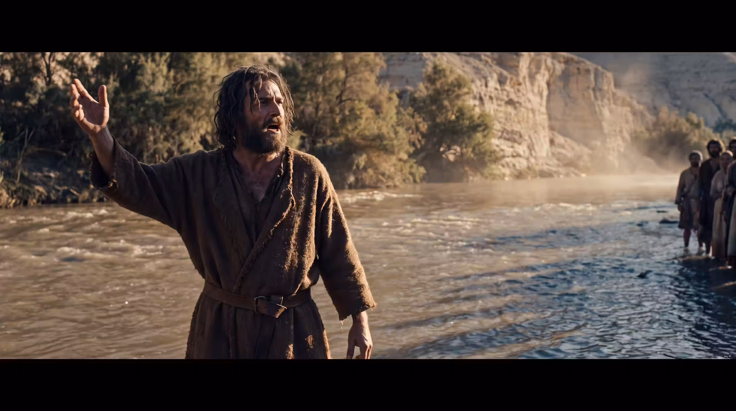 A gaunt man in a camel-hair garment standing knee-deep in the Jordan with one arm raised, a few people waiting in the shallows