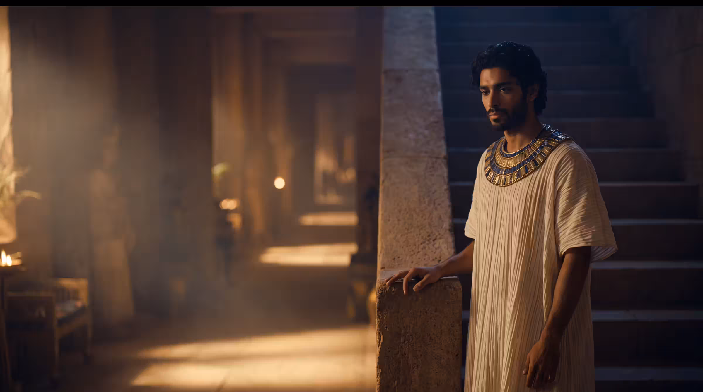 Joseph at the head of a broad palace stair in Memphis, a hand on the balustrade, the lamplit hall receding below