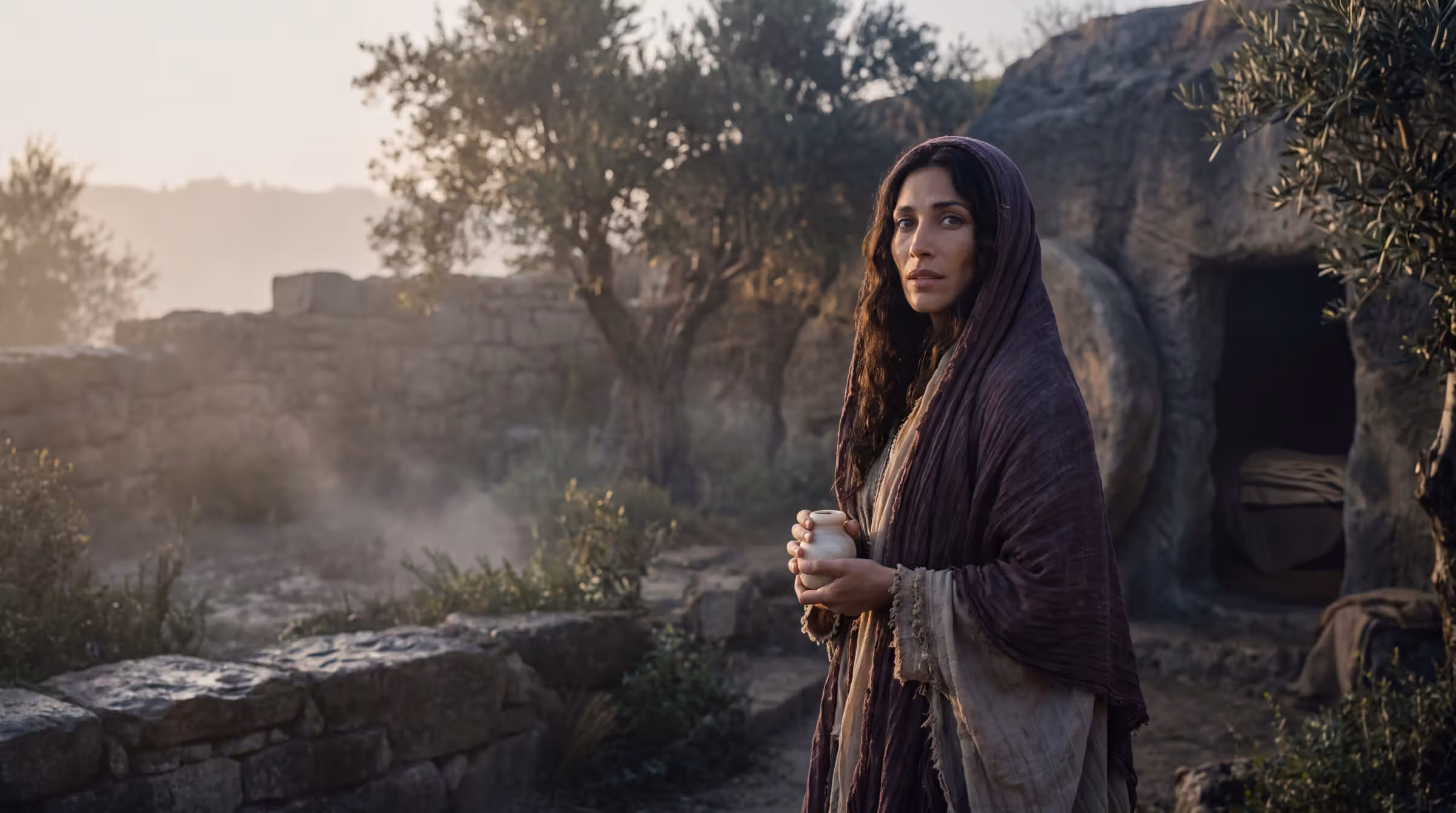 Mary Magdalene turning in a walled garden at sunrise, an alabaster jar in her hand, the open tomb in the hillside beyond