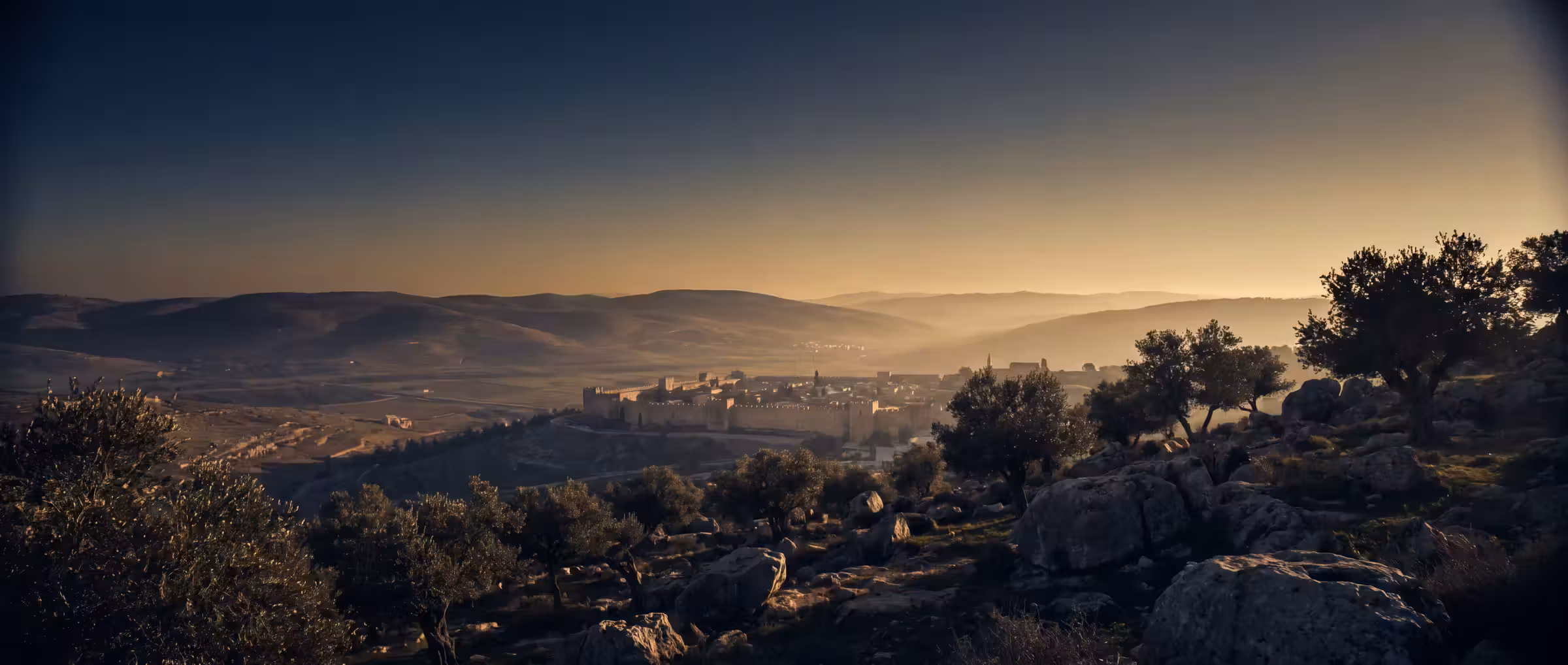 An ancient walled city in a valley at sunrise, seen from a hillside